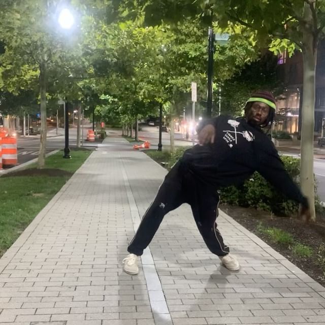 Toughjohnnie dancing on an esplanade walk under street lights, posed in an intense lean to the side.